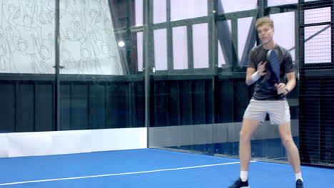 young man playing padel tennis, swinging racket on indoor court