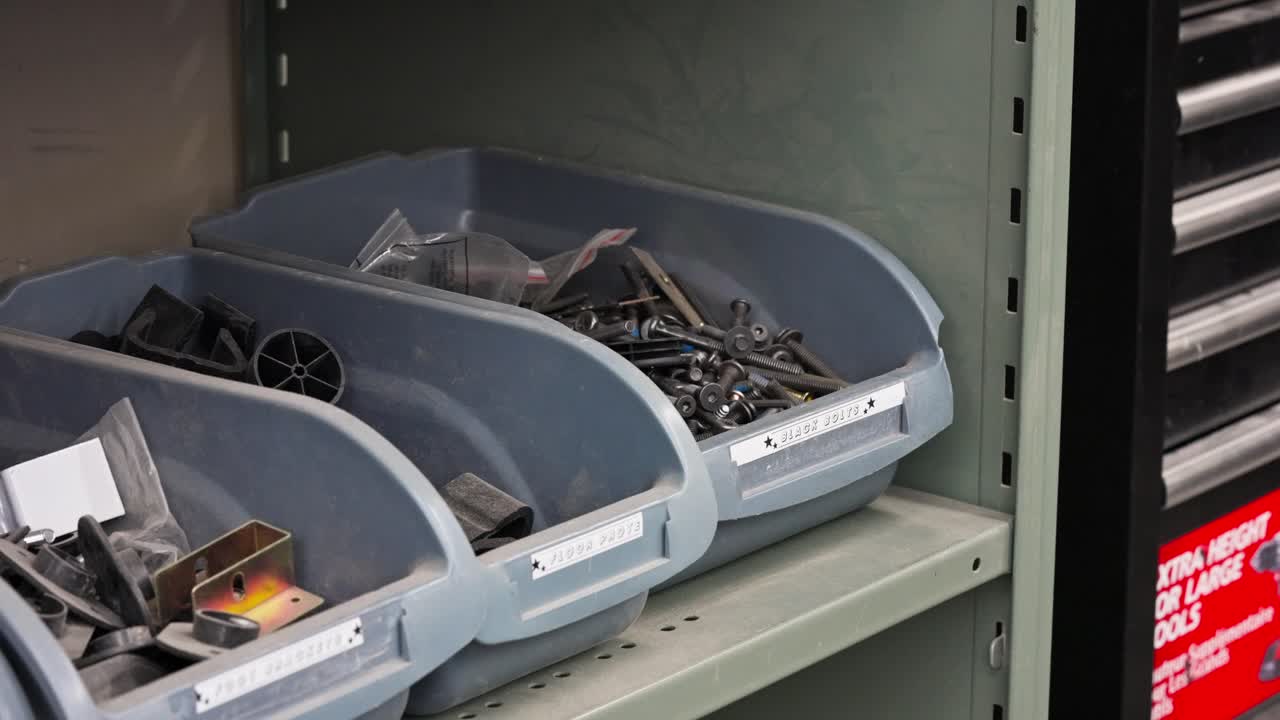 Close high-angle pan across labeled bins showing screws, bolts, and parts