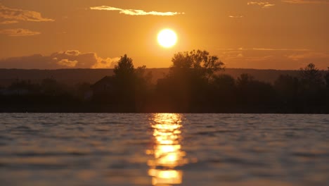 lakeside landscape with dark silhouette of park trees reflicted in lake water and distant walking pedestrian people on embankment at bright sunset