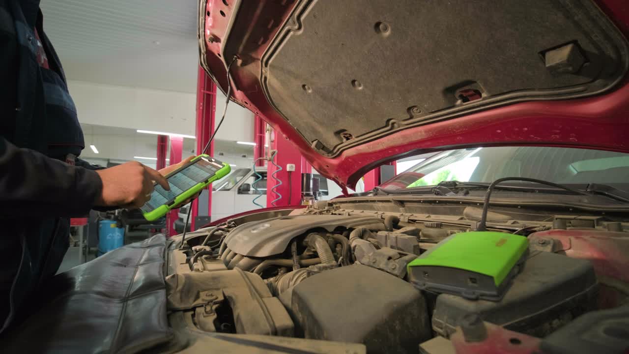 el electricista o mecánico de servicio de automóviles utiliza una tableta con software de diagnóstico interactivo futurista. inspeccionando el vehículo para encontrar componentes rotos en el compartimento del motor del automóvil moderno