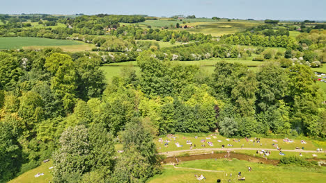 a uk countryside park viewed from a drone—people relish a meandering stream, picturesque picnic locales, and a wooded tourist attraction