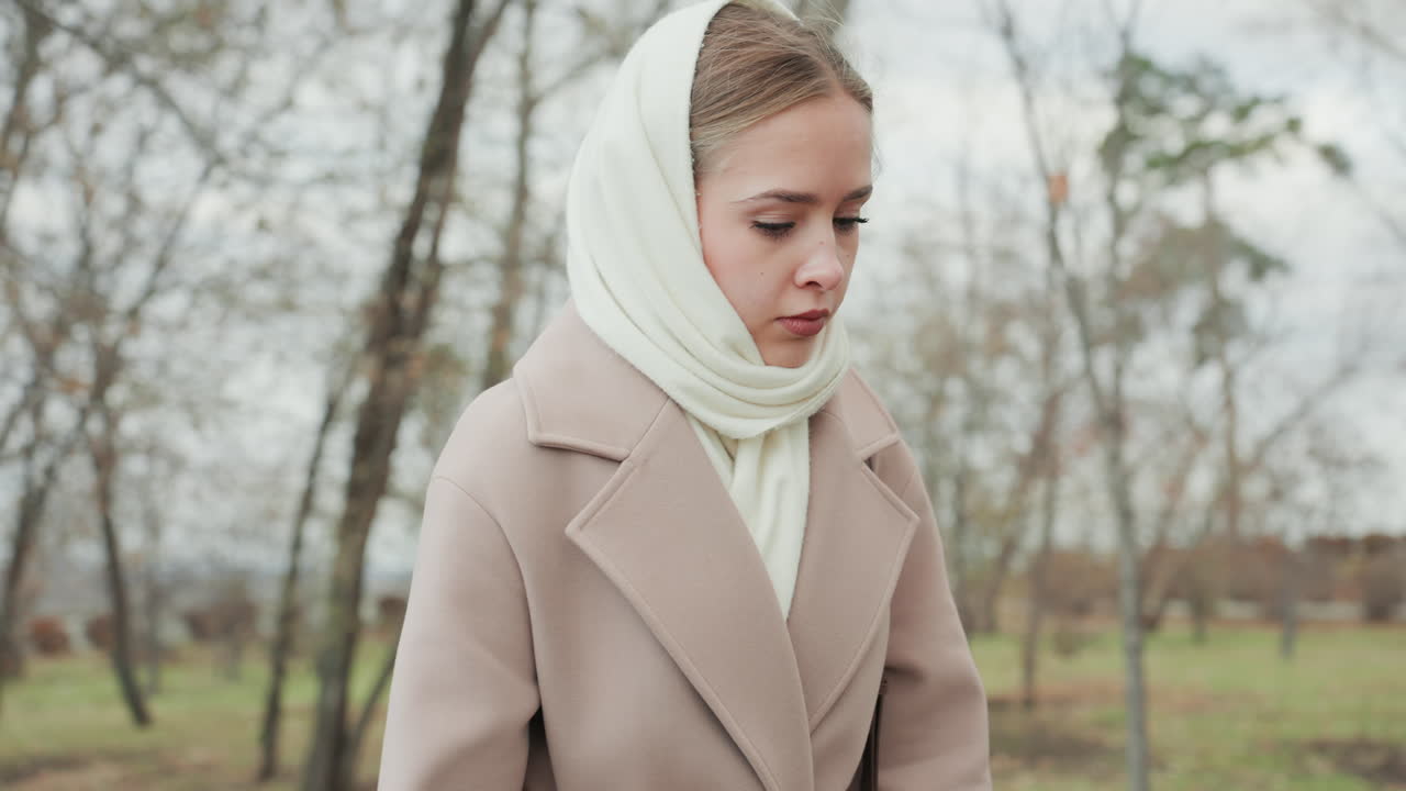 Giovane donna che passeggia. Una giovane donna bianca si muove lentamente tra le foglie autunnali in una giornata nuvolosa. Una giovane donna caucasica con borsa a tracolla percorre un sentiero del parco tra il fogliame autunnale e il vento fresco.