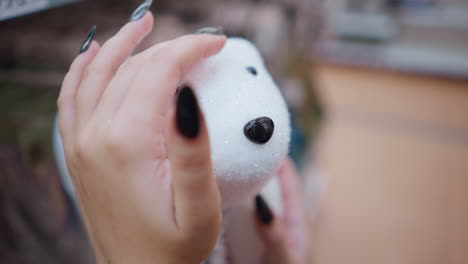 close-up of a person's hand with black polished nails tenderly holding a white plush polar bear, highlighting the sparkling details against a softly blurred background