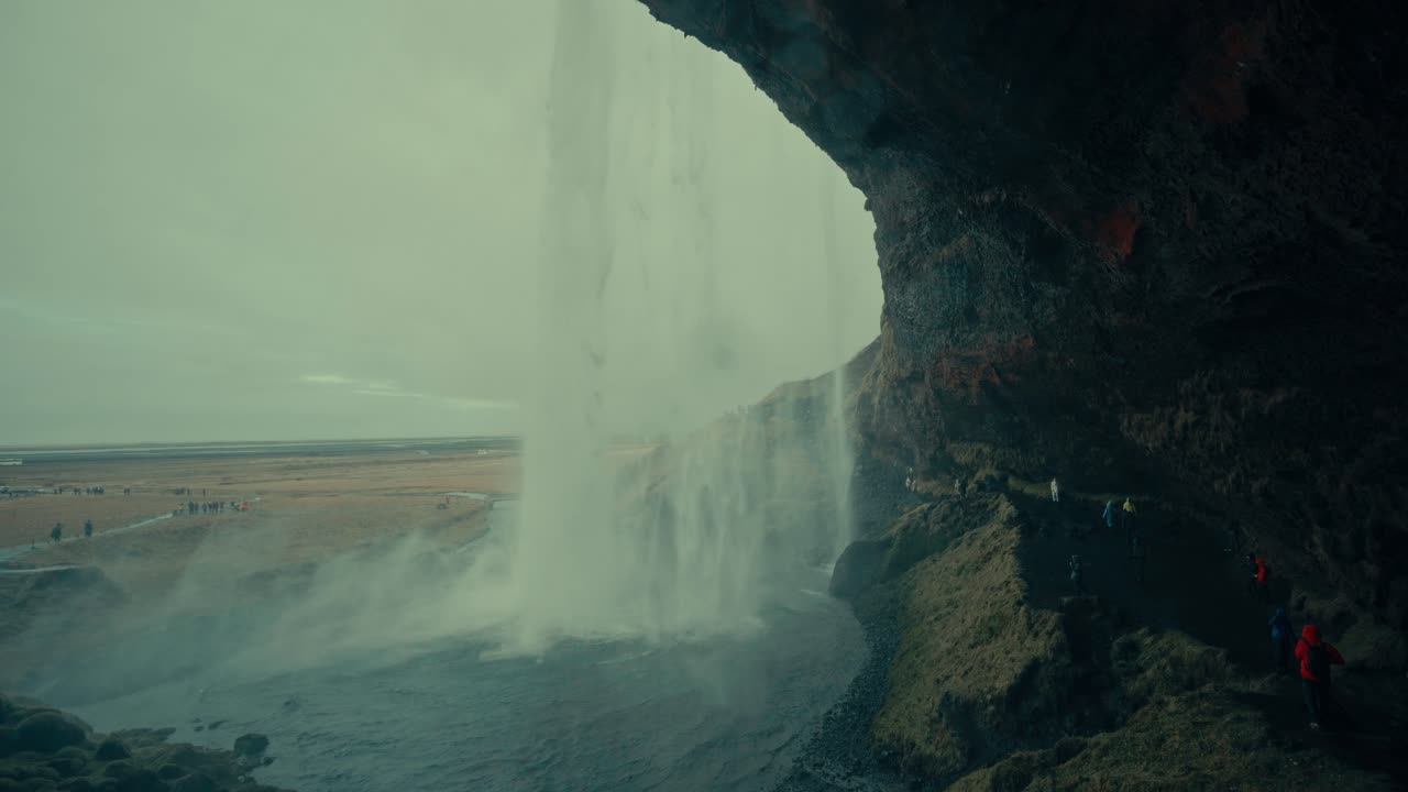 Turistas caminando detrás de la majestuosa cascada Seljalandsfoss en Islandia.