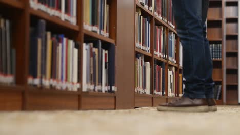 toma en ángulo bajo de las piernas de una persona caminando mientras se detiene para buscar un libro en la biblioteca