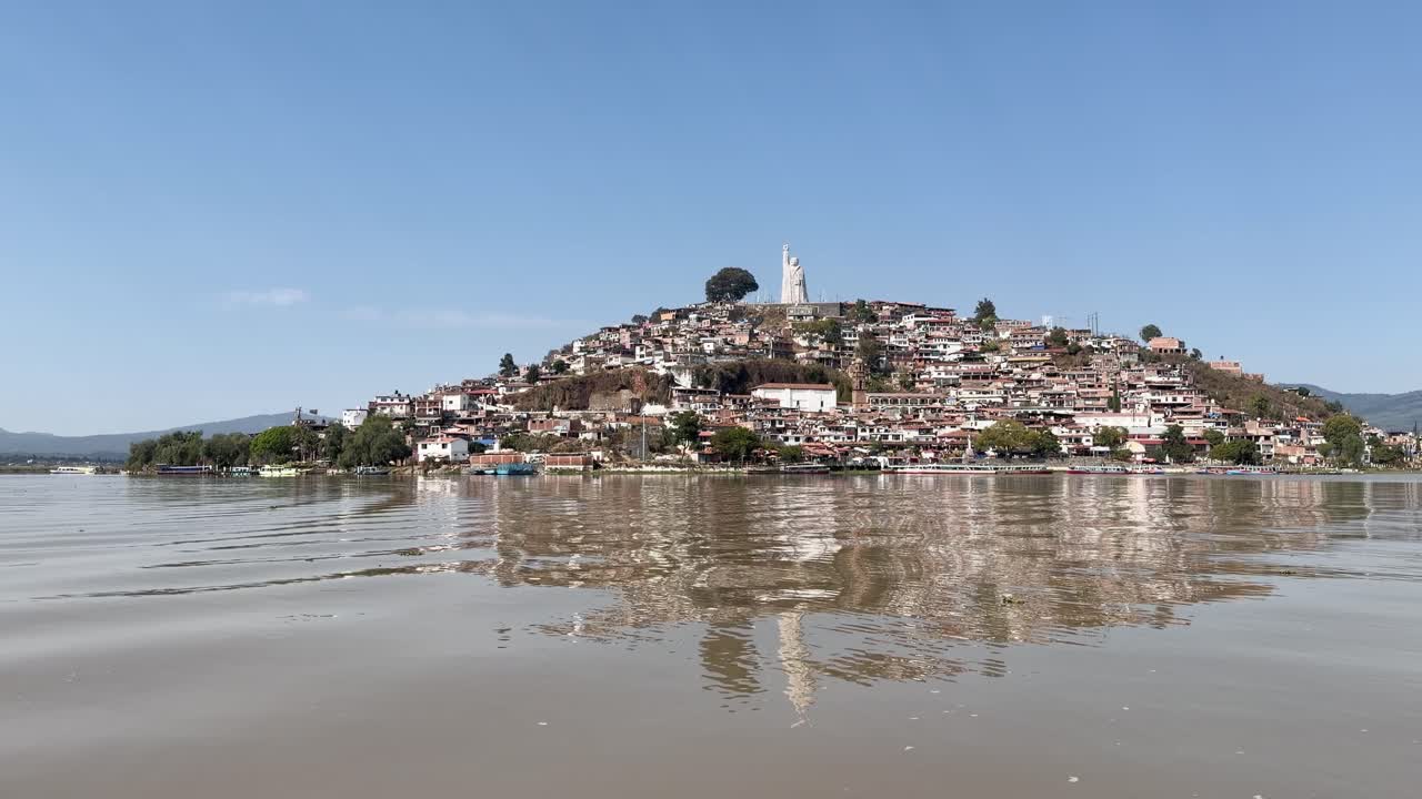 Vista serena da Ilha Janitzio refletindo em um lago tranquilo sob céus azuis.