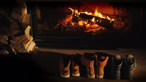 a few pairs of winter shoes are drying near the fireplace where the fire is on