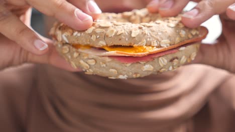 person eating a ham and cheese bagel