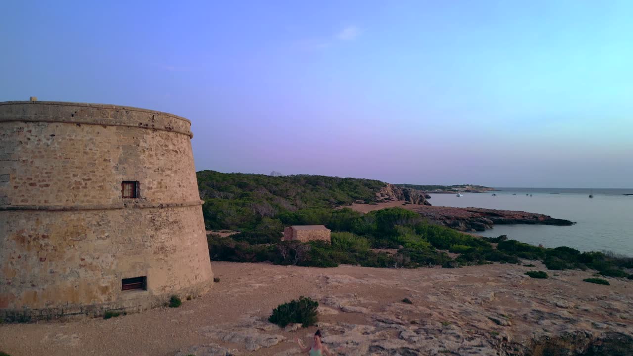 Barefoot hippie girl practicing yoga at sunset near Torre des Carregador, Ibiza, Spain. speed ramp hyper motion time lapse. ascending drone