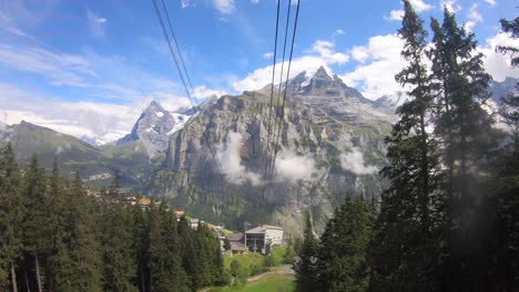 Gondola-ride:-ascent-in-the-swiss-alps-with-a-landscape-on-the-alps,-rocky-mountains,-fir-tree-forest-and-green-valleys,-gondola-poles-support-the-cable