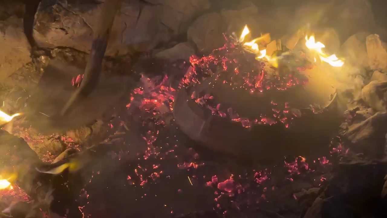 Glühende Glut und Flammen umgeben eine glockenförmige Haube, die nachts an einem Berg-Lagerfeuer zum Kochen von Speisen verwendet wird.