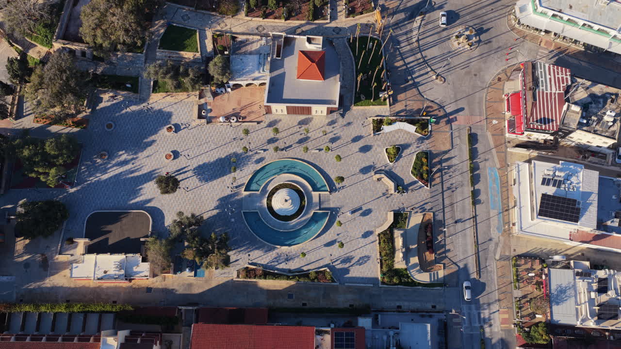 Veduta aerea con drone di una piazza con fontana circolare circondata da strade ed edifici ad Ayia Napa, Cipro, che mostra una pulita geometria urbana.