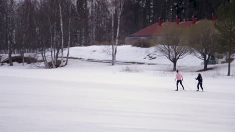 two people in warm winter clothes skiing past on vast snowy area towards a large forest area in vuokatti finland