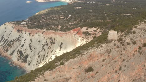 Ibiza-pirate-tower,-aerial-view-over-the-old-watch-tower-with-the-island-of-Ibiza-in-the-background