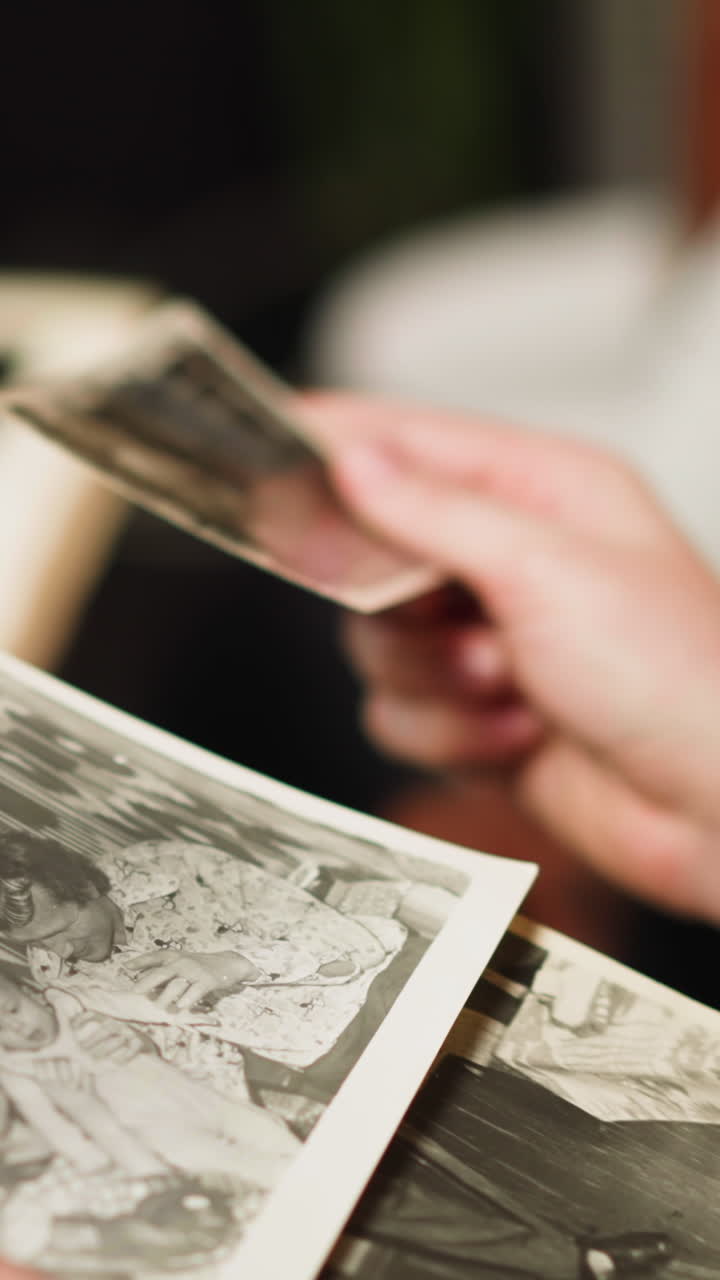 Woman looks at old faded black and white family pictures in photo album sitting near little daughter and husband in living room closeup slow motion