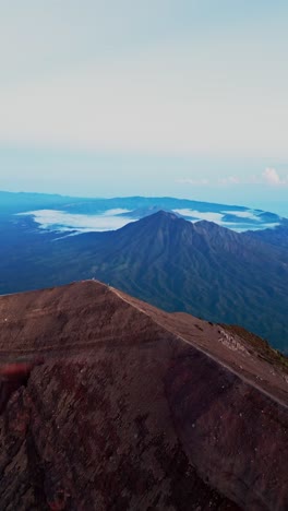 mount agung summit seen from a vertical drone offers a stunning perspective of bali's highest volcano with its smoky crater rocky terrain and panoramic views across the island.