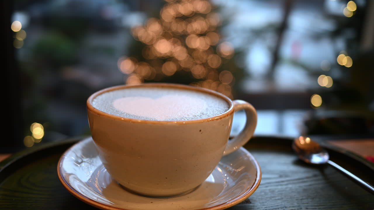 Cup of coffee with foam latte art in heart shape. Christmas tree on background