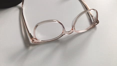 Modern-eyeglasses-in-light-colour-lie-on-a-white-table,-bright-glasses-frame,-slow-motion-footage