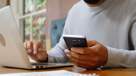 Man-using-mobile-phone-and-laptop-in-cafeteria-4k