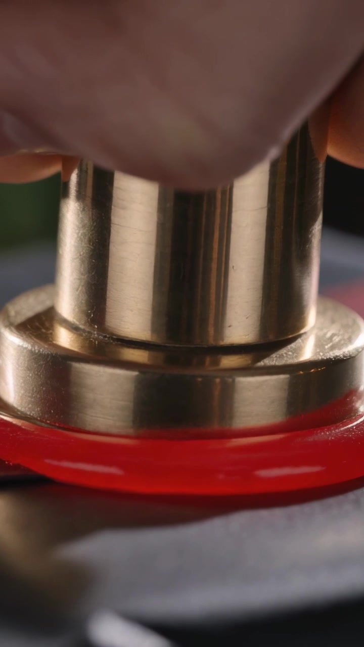 Vídeo vertical: Polegar em movimento, mão nua pressionando um êmbolo em uma base preta, apertando um anel vermelho, encaixando.