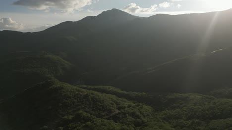 flyover of misty lush green mountain jungle, lens flare from low sun