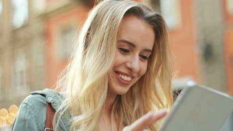 close-up view of blonde young woman making a video call on the tablet and walking down the street