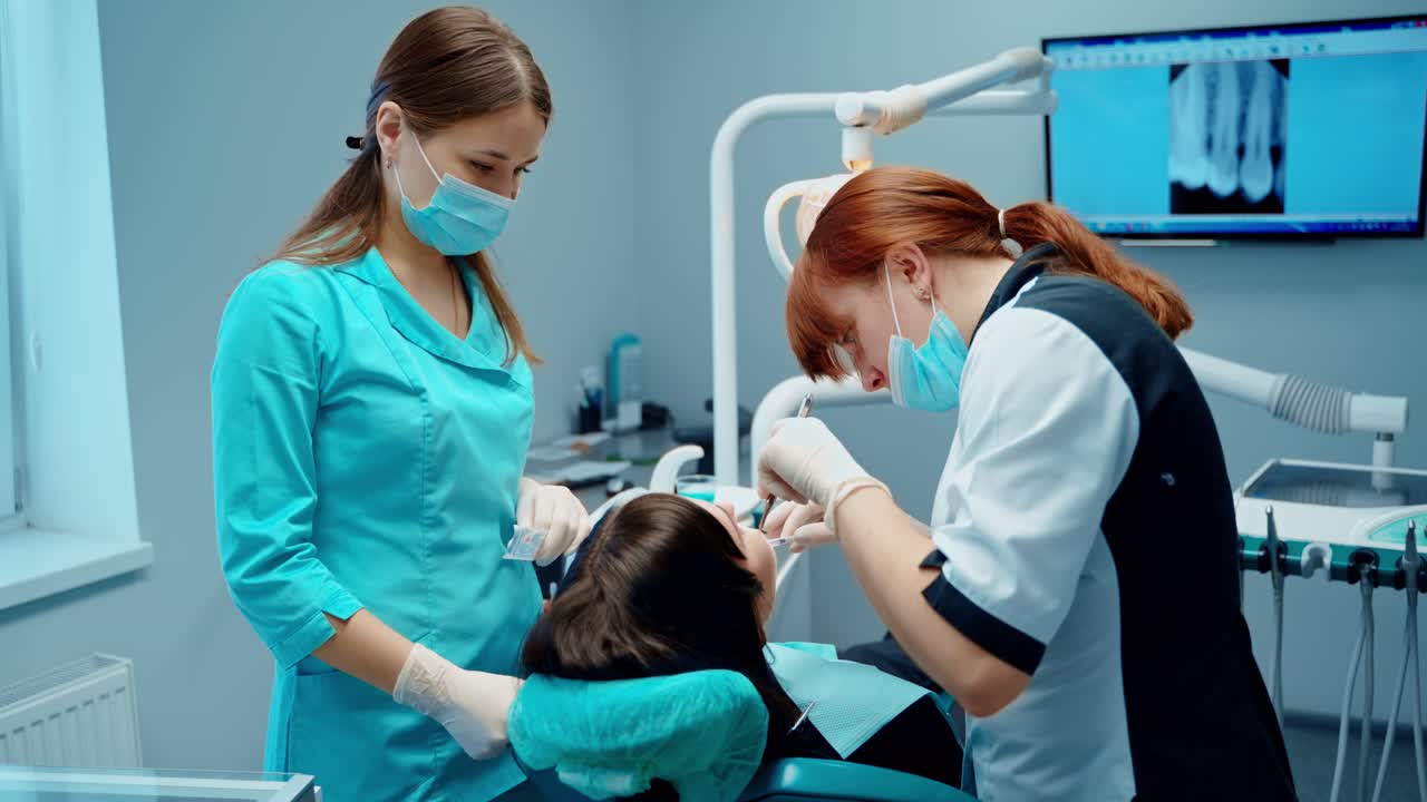 Dentist with assistant treat patient's teeth. Dental procedure in the modern stomatology office. Female dentist working in patient oral cavity.