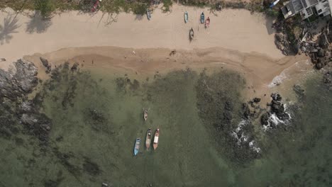 Fishing-boats-moored-in-shallow-water-off-rocky-sand-beach,-aerial