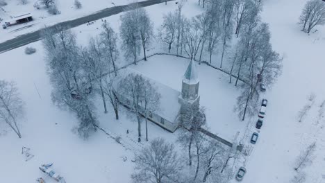 snow-covered church in renda village with surrounding bare trees, aerial view, moving forward, tilt down