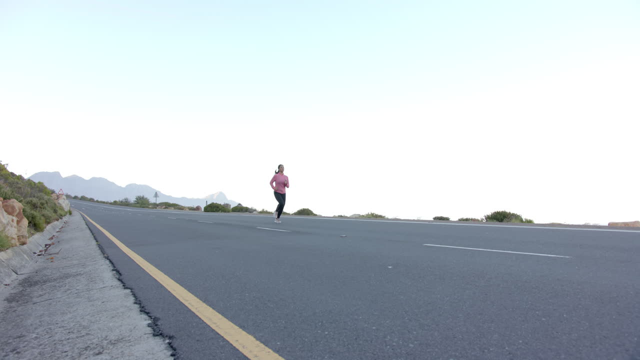 Running on empty road, woman exercising outdoors with mountains in background, copy space