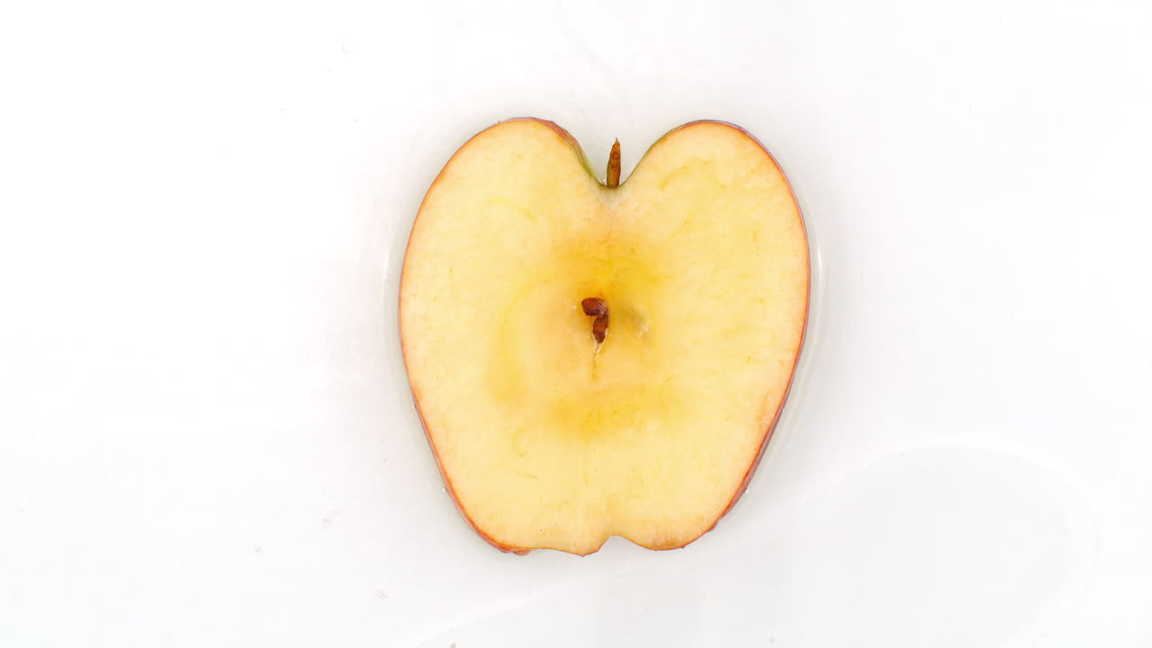 I slowmotion sprøjter vand på et æble på en hvid baggrund. Vegetar og fruktarer.