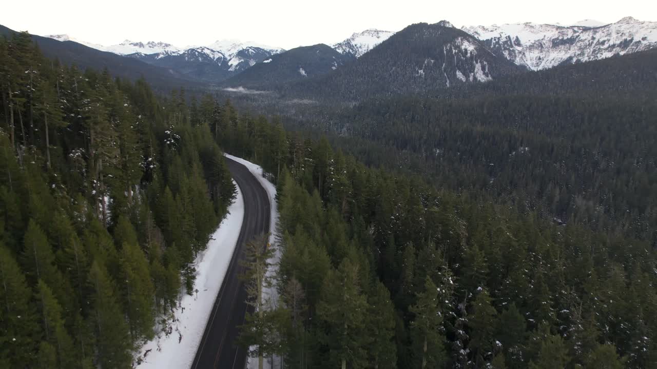 Mountain Pass in winter with light snow on ground and green pine trees- aerial ascending