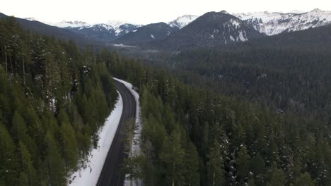 mountain pass in winter with light snow on ground and green pine trees- aerial ascending