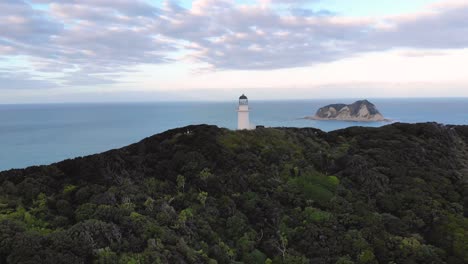 Aerial-orbit-of-East-Cape-Lighthouse-located-on-forested-hill,-East-Coast,-Gisborne-District,-New-Zealand