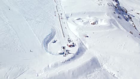 aerial view looking down over winter tourists starting to ascend ski resort lift on steep snow covered mountain slope