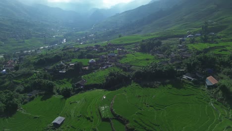 wide aerial pan right of rice terraces and rural buildings surrounded by misty mountains