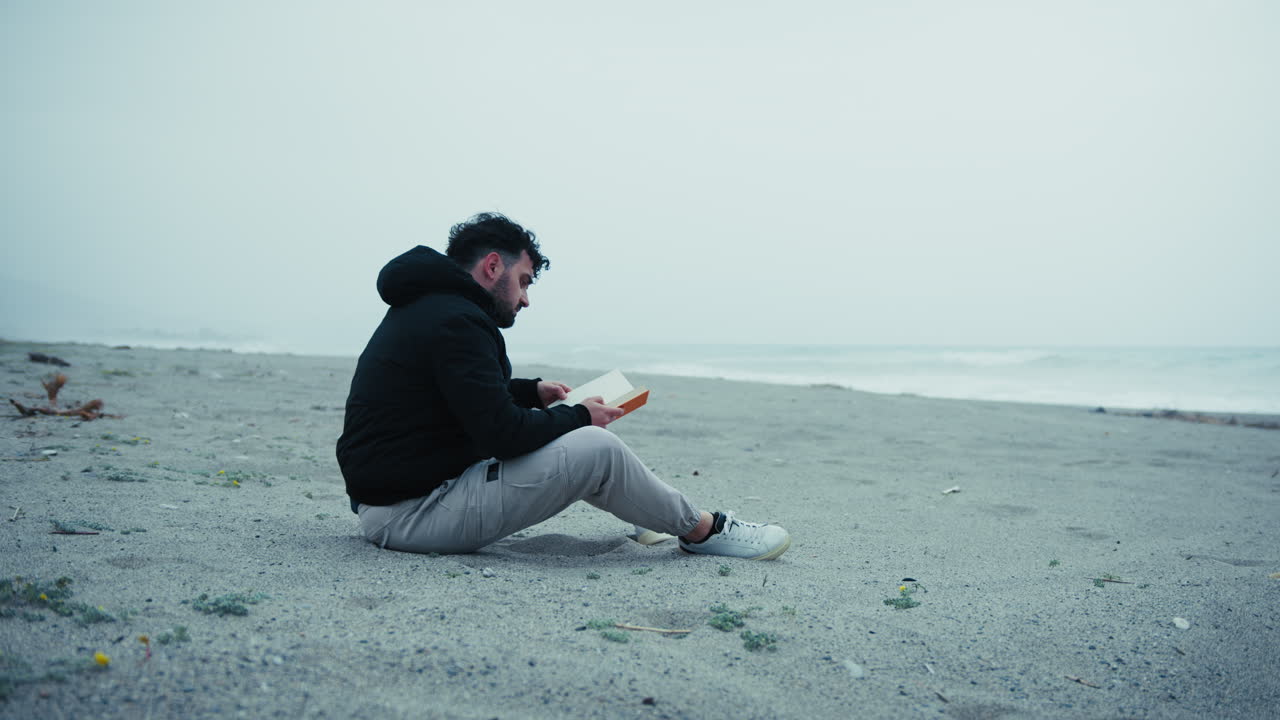 Sad Man Starts Reading A Book Sitting On The Sand In Winter