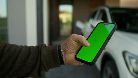 persona sosteniendo un teléfono inteligente con una pantalla verde frente a un coche en un garaje.