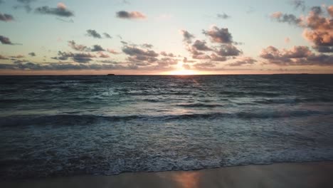 Drone-Shot-starting-on-the-beach-and-flying-towards-a-beautiful---colorful-Hawaiian-Sunrise-off-of-the-North-Shore-coast-of-Oahu,-Hawaii