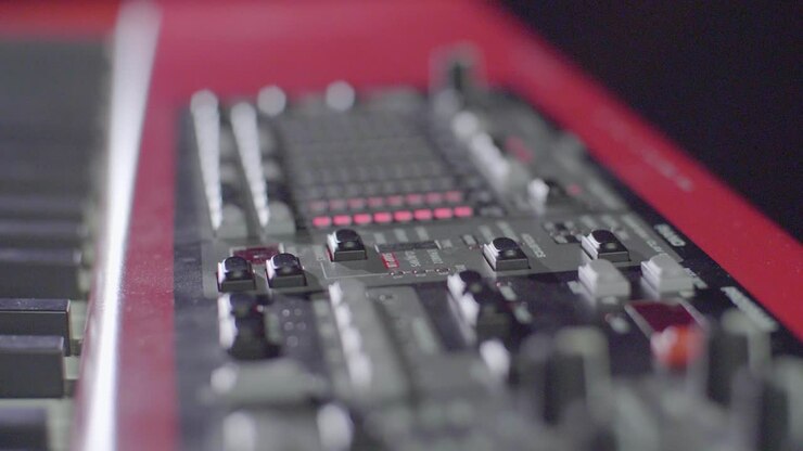 Slow motion close up of an electric stage piano synthesizer keyboards buttons, knobs and faders blinking red with led stage light scenery