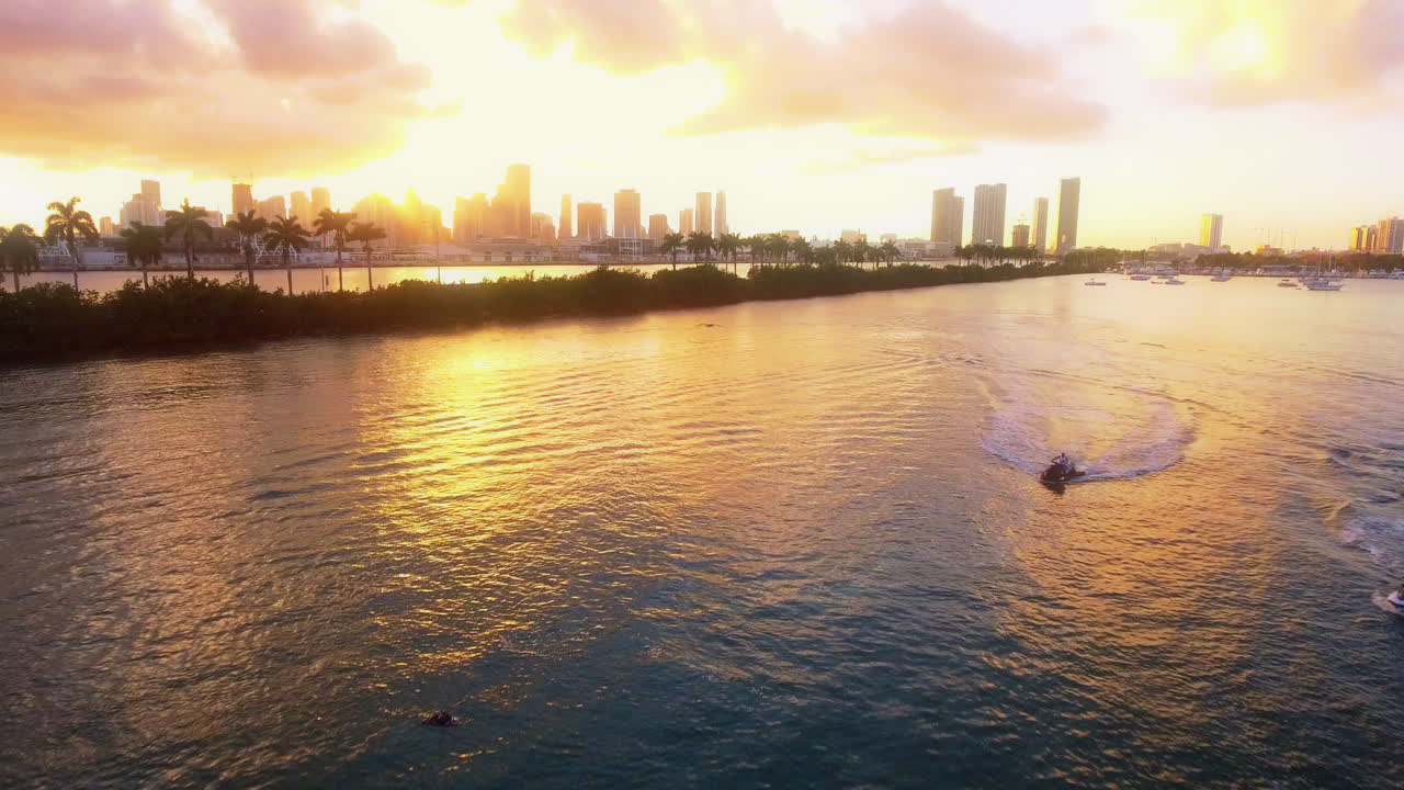 Vista de drones de motos acuáticas cruzando la Bahía de Biscayne con el horizonte de Miami brillando al atardecer