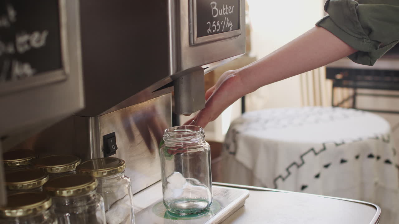 close up de una mujer llenando un recipiente con mantequilla de maní en una tienda de comestibles sostenible sin plástico
