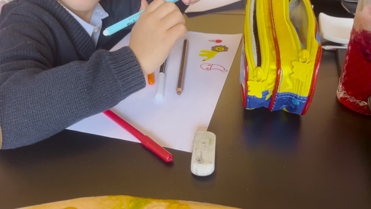 Young child writing on paper at a desk with colored pens and books, creative workspace and playing to relax and learn