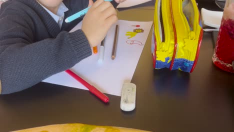 young child writing on paper at a desk with colored pens and books, creative workspace and playing to relax and learn