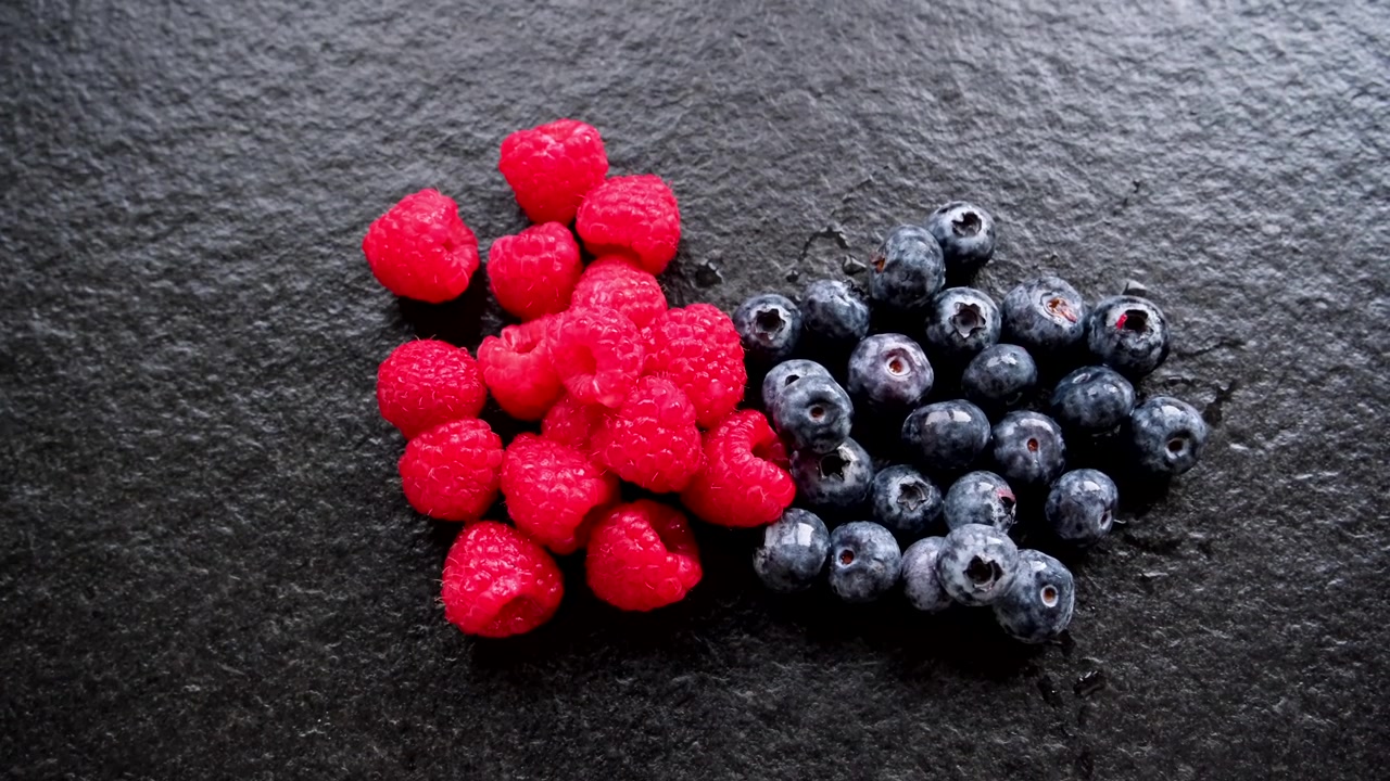 Vibrant colors of fresh newly harvested raspberries and blueberries are placed on top of the black texture kitchen counter