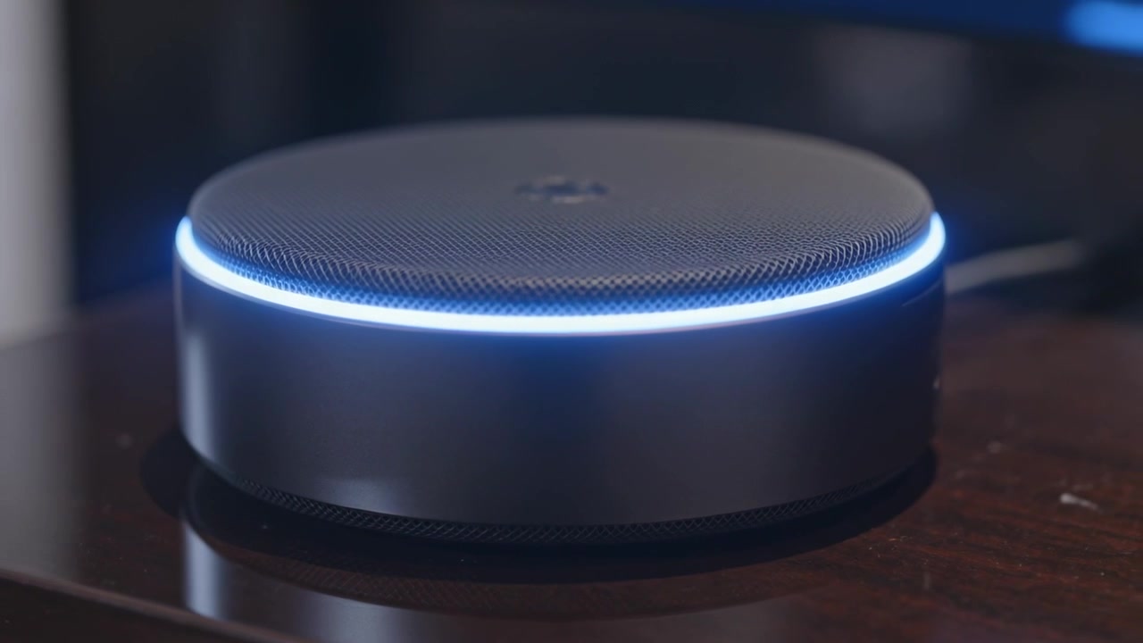 La telecamera panoramica rivela un altoparlante intelligente con un anello LED che si illumina, indicando lo stato attivo su una scrivania di legno.