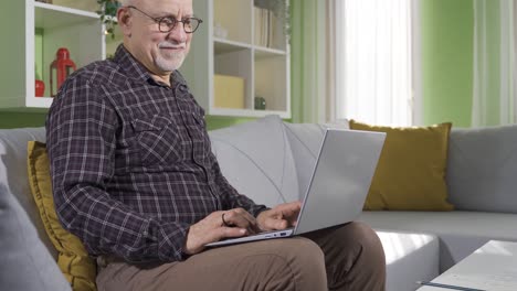 Old man at home using laptop and smiling, having fun and cheerful.