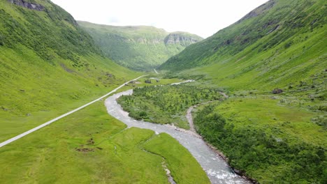 Auto-Fährt-Auf-Geradliniger-Straße-In-Einem-Wunderschönen,-Ruhigen,-Idyllischen-Und-üppig-Grünen-Tal-Mit-Fluss-Am-Berg-Vikafjell-In-Der-Nähe-Von-Voss,-Norwegen---Luftbewegung-Vorwärts-Und-Seitwärts-In-Richtung-Straße-Rv13