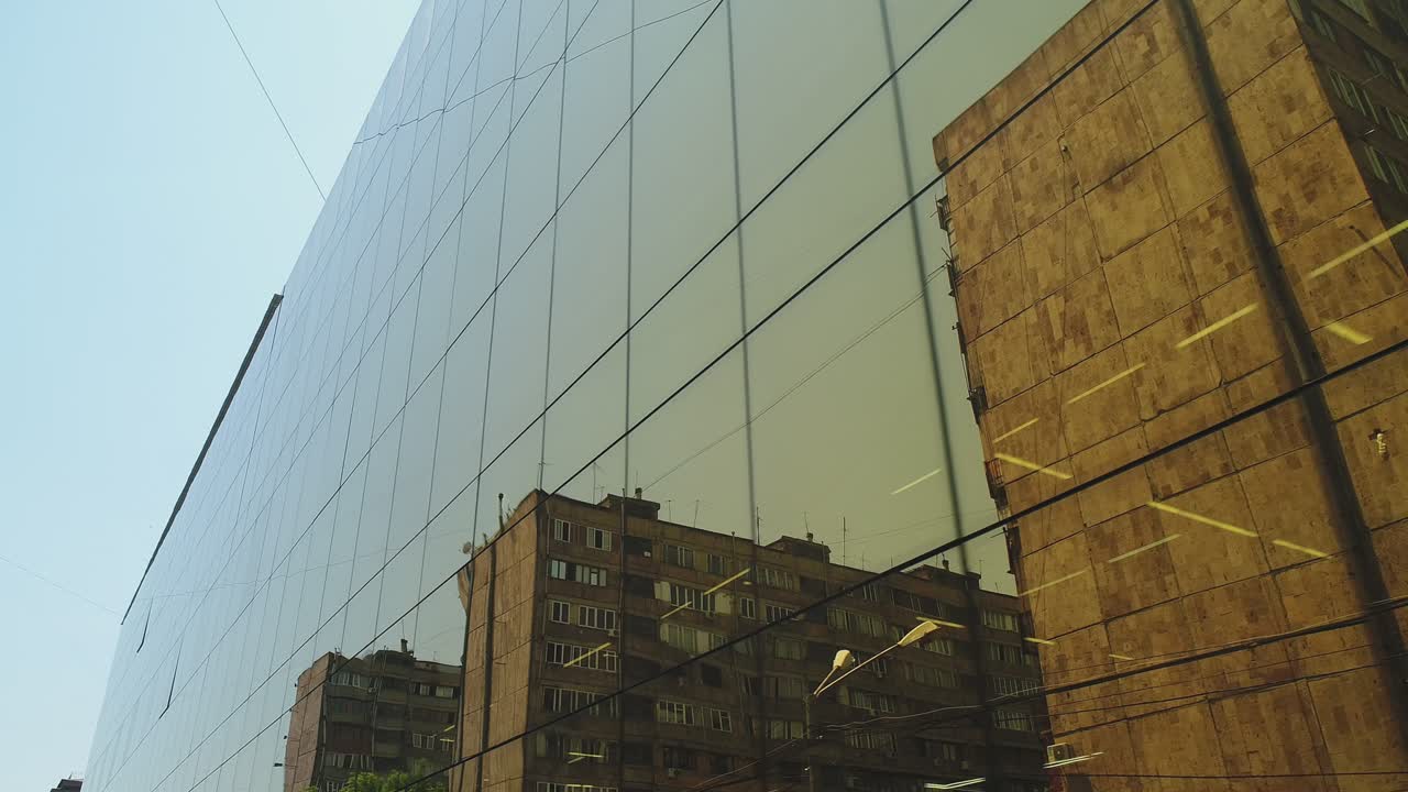 vista exterior de 4k de un edificio del distrito comercial o un centro comercial con ventanas de espejo de pared durante el día. luz solar. reflejo de la ciudad, coches y torres en paredes de espejo. cámara de avión no tripulado en movimiento