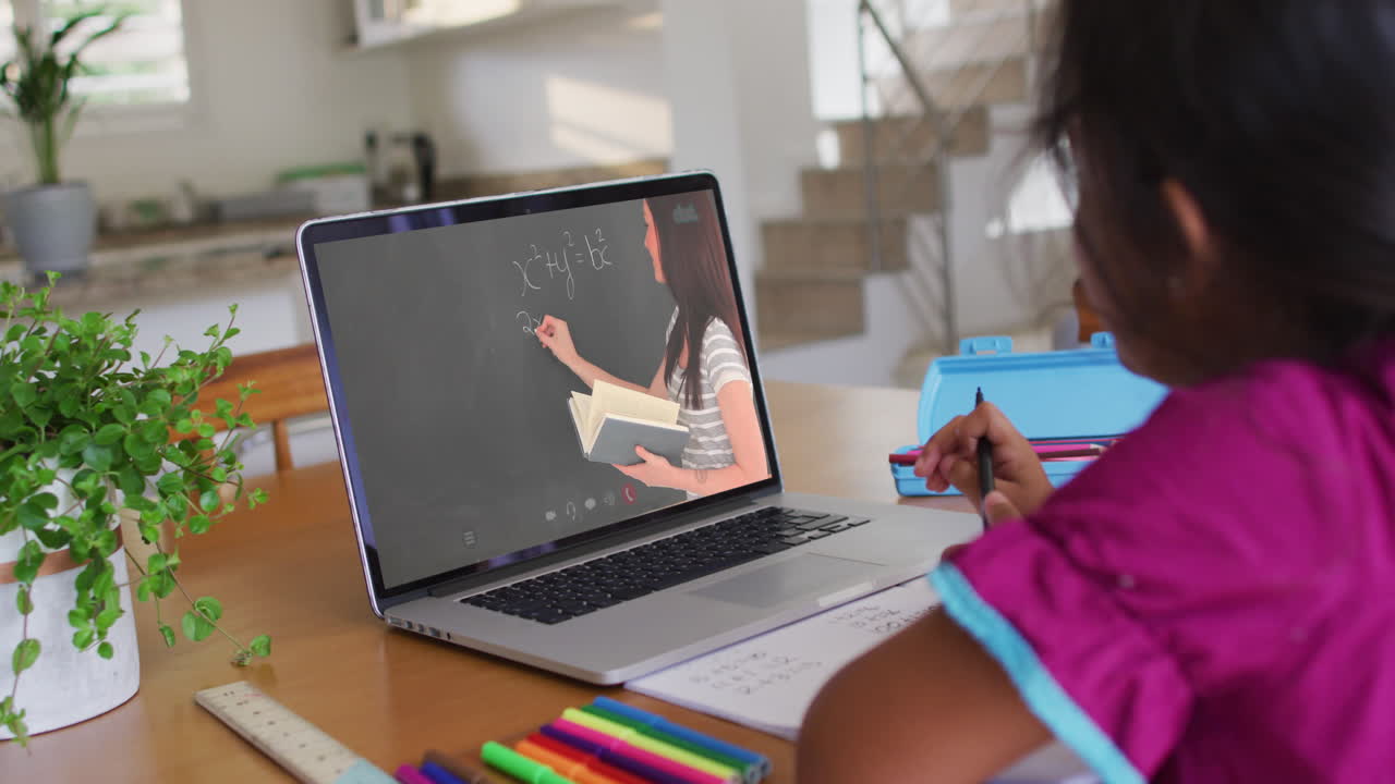chica afroamericana haciendo la tarea mientras hace una videollamada en una computadora portátil en casa